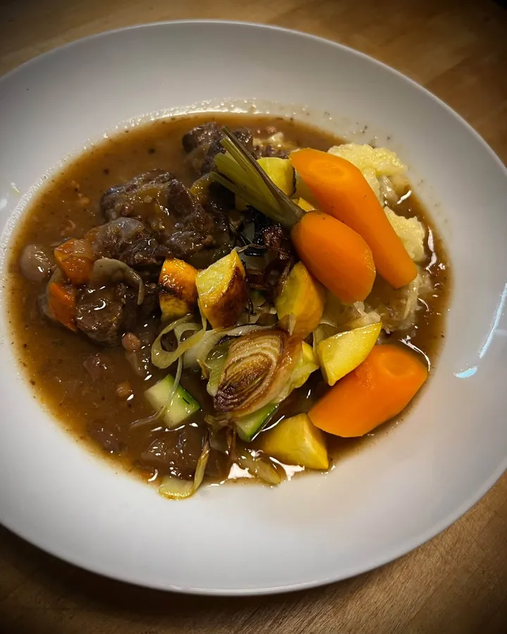 Bœuf mijoté dans une sauce riche, avec carottes glacées, courge rôtie, oignon grillé et écrasé de pommes de terre