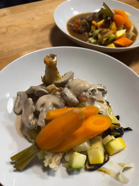 Poulet à la crème et aux champignons avec carottes et légumes, un bol de bœuf mijoté derrière