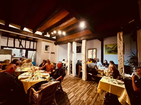 La salle pleine de convives sous les poutres apparentes, avec des nappes vichy jaunes