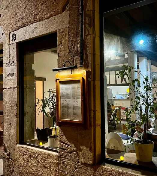 Le 5 R la nuit : la façade en pierre du numéro 18, une carte éclairée, et des convives attablés près de la fenêtre