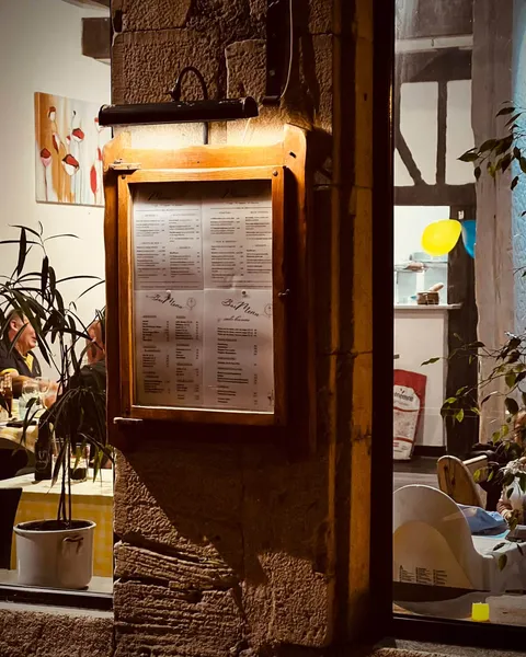 Le panneau du menu en bois éclairé sur le mur de pierre, avec des convives derrière la vitre