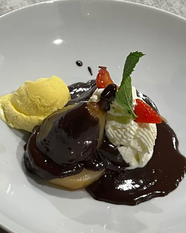 Poire pochée nappée de chocolat noir, avec glace à la vanille, crème fouettée, fraise et menthe