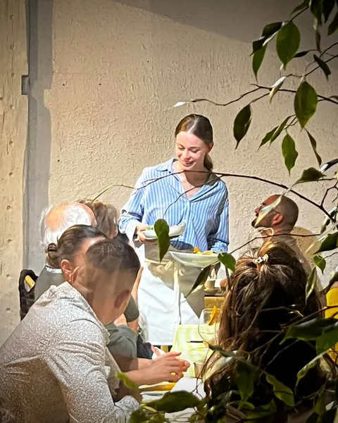 Une serveuse apportant les assiettes à une table animée, vue à travers le feuillage