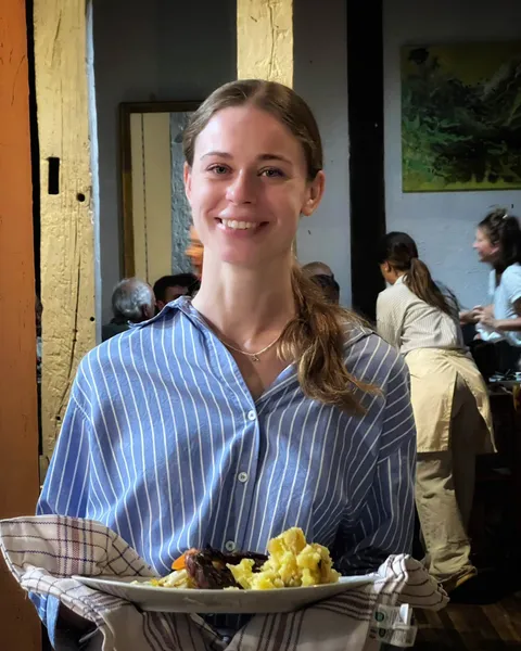 Une serveuse souriante en chemise rayée portant une assiette de steak et d’écrasé de pommes de terre